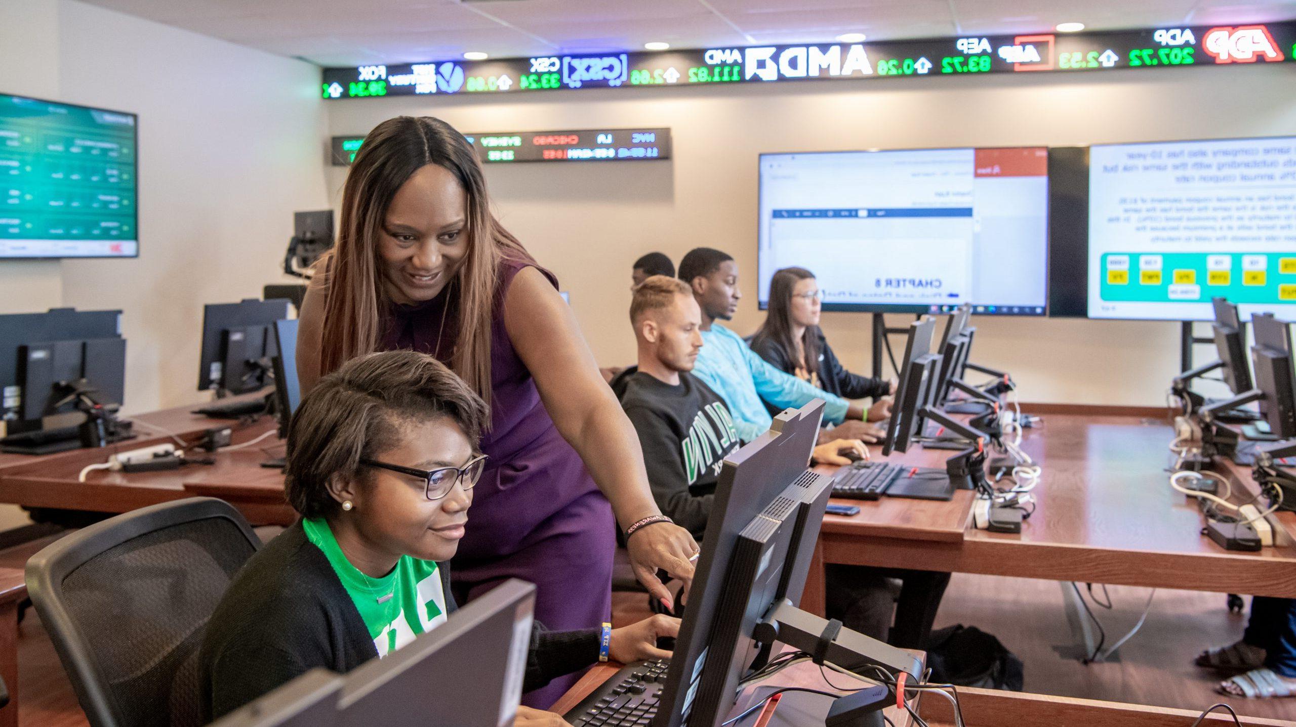 Professor pointing at students computer screen in finance class lab.